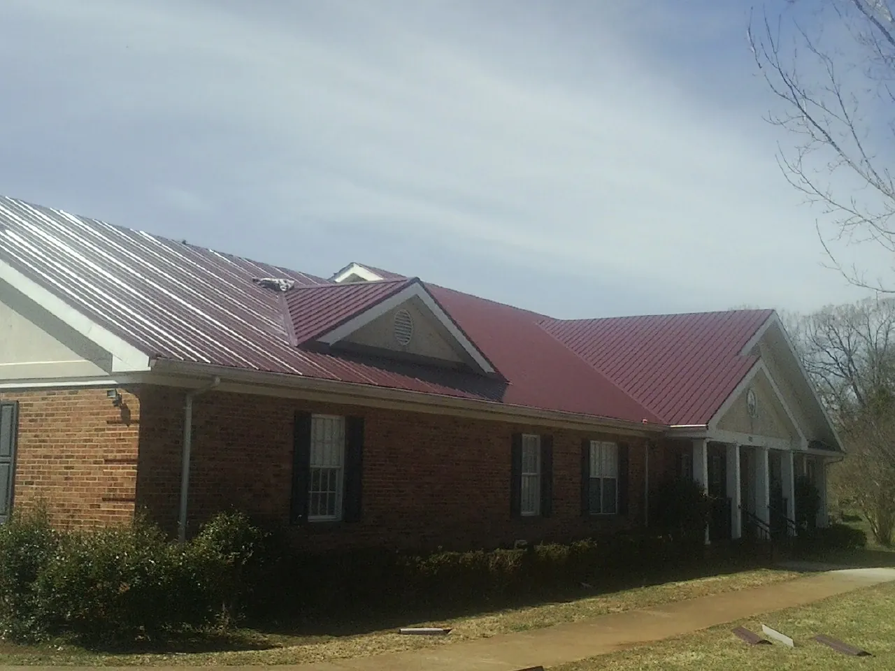 Red metal roof with gabled entries on a long brick building, from a Hail Damage Roof Repair job in Bayport