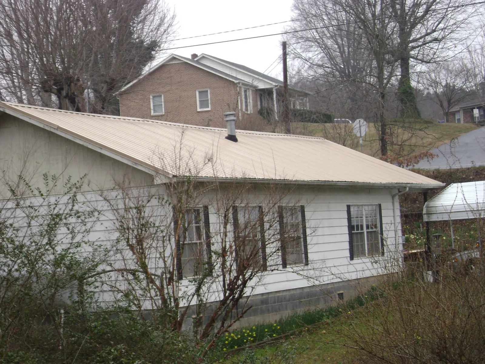 Tan metal roof on a white sided house set into a hillside — Commercial Roofing by Roofing Brothers in Bayport